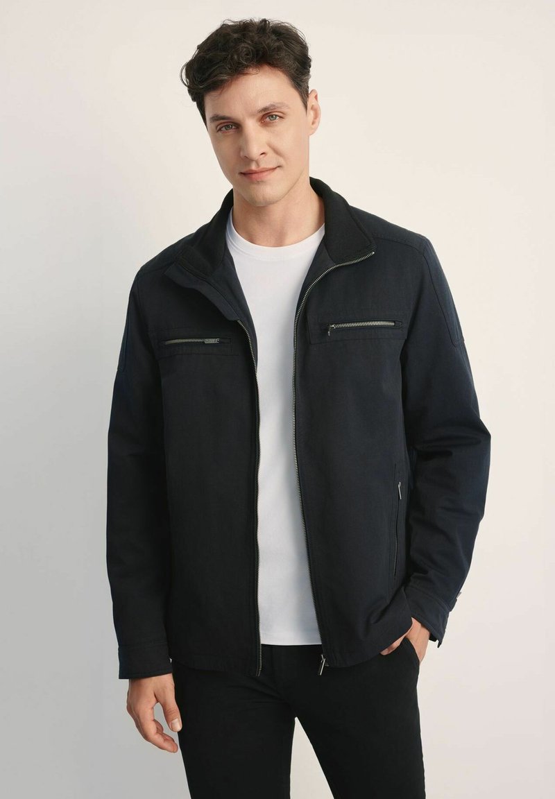 Czarna kurtka z zamkiem z przodu, dwoma kieszeniami na piersi i kołnierzem. Wykonana z gładkiego materiału, o minimalistycznym designie i dopasowanym kroju.