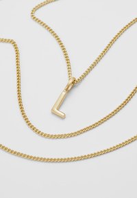 Halskette aus goldfarbenen Ketten mit einem geometrischen L-förmigen Anhänger. Die Kette ist gedreht und der Anhänger ist glatt mit einer polierten Oberfläche.