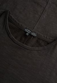 T-shirt en coton noir avec un col rond, une texture douce et un bord côtelé subtil. Étiquette de la marque visible près du col.
