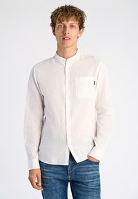Witte, lange mouwen linnen shirt met een geknoopte kraag, enkele borstzak en een relaxte pasvorm. Gecombineerd met blauwe denim jeans.