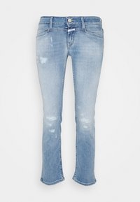 Jeans de denim azul claro desgastado con parches rasgados y una cintura de tiro medio, exhibidos sobre un fondo blanco liso.