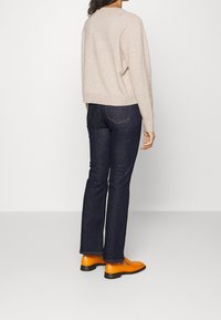 Un pull en tricot beige, un jean bleu foncé et des bottines orange vif. L'ensemble est simple, avec des coutures visibles et une texture denim standard.