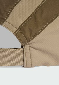 Béžový a olivově zelený látkový pásek má texturované panely, prošité švy a hladký, odolný povrch. Součástí je nastavitelný tkaný popruh.