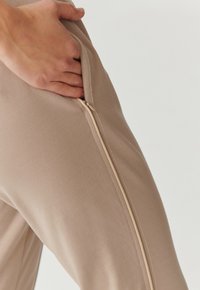 Slim-fit beige broek van zacht materiaal, met een subtiele zijrits en een gladde textuur, met een minimalistisch ontwerp.