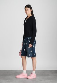 Zwarte geribde cardigan, denim shorts met bloemenapplicatie, roze platform sneakers, witte sokken, en een kleine roze handtas.