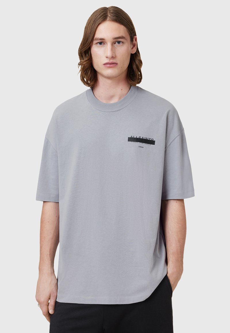T-shirt surdimensionné gris clair en coton doux. Avec un col rond et un logo imprimé sur la poitrine gauche. Manches courtes.