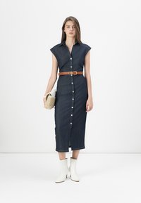 Jeanskjole med korte capærmer, knaplukning foran, bælte i taljen og knælang skørt; parret med hvide ankelstøvler og en clutch-bag.