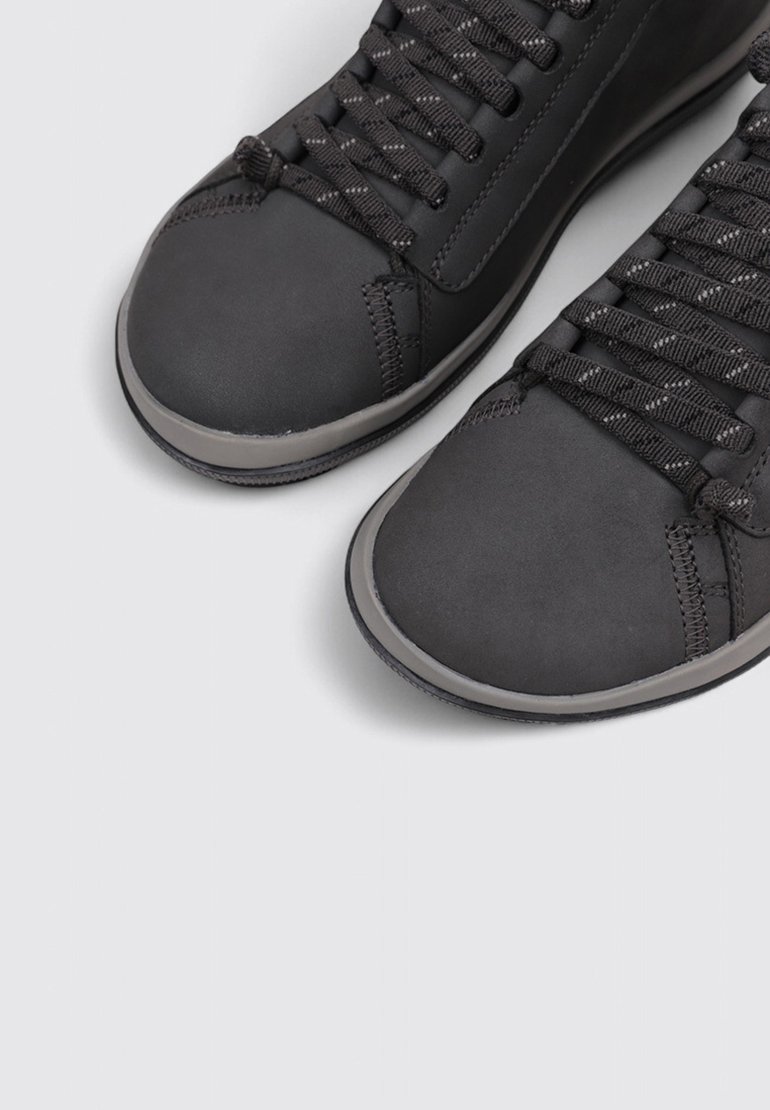 Black sneakers with a matte finish, rounded toes, textured surfaces, and contrasting gray rubber soles. Features flat black laces.