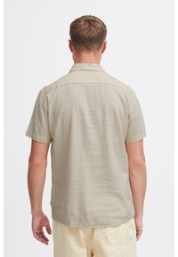Kortærmet, lys beige skjorte med knapper lavet af tekstureret stof. Har en spids krave og en afslappet pasform med en lige kant.