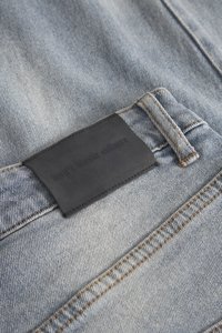 Lichtblauwe denimstof met een licht vervaagd structuur, met een zwart leren label genaaid op de tailleband met geperst tekst.