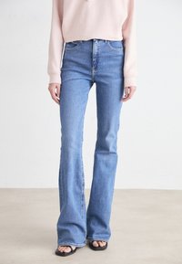 Jeans acampanados azules de cintura alta, fabricados en denim, que presentan un diseño clásico de cinco bolsillos, un ligero deslavado y un corte recto en el muslo.