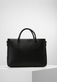 Sac fourre-tout en cuir noir avec deux poignées supérieures. Présente une forme rectangulaire élégante et une texture lisse. Aucun matériel visible ni motifs.