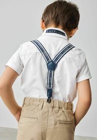 Mornarske nastavljive naramnice pripete na belo srajco, nosene čez khaki hlače z oznako na hrbtni strani in žepi na obeh straneh.