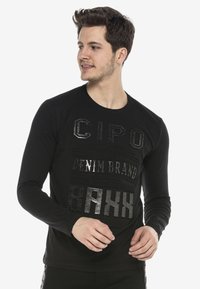 Schwarzes Langarm-T-Shirt mit strukturiertem, reflektierendem Text in verschiedenen Schriftarten auf der Vorderseite, Rundhalsausschnitt und enganliegende Ärmel.