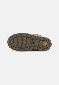 Semelle extérieure en caoutchouc marron avec des sculptures profondes, présentant une texture striée et un accent de logo circulaire. Renforcée pour la durabilité et l'adhérence.