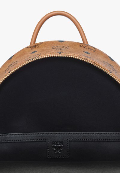 Sac en cuir brun en forme de dôme avec une fermeture éclair en or, présentant des motifs gaufrés et un intérieur noir, mettant en avant une étiquette en cuir de marque.