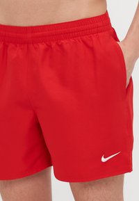 Røde Nike-shorts med elastisk linning, sidelommer og en hvit logo på venstre ben, laget av glatt og lett stoff.