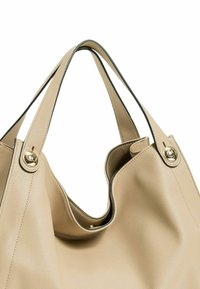 Borsa a tracolla in pelle beige con texture liscia, apertura superiore arrotondata e dettagli in metallo dorato sulle cinghie. Design minimalista.