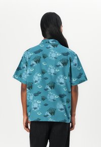 Korte mouwen shirt in teal stof, met verschillende zwierende patronen, zwarte ruimteschipmotieven en een ontspannen pasvorm met een kraag.