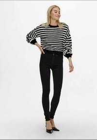 Pull rayé noir et blanc à manches longues, associé à un jean skinny noir taille haute et des talons aiguilles noirs.
