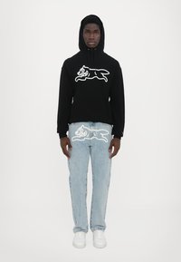 Hanorac negru cu un grafic de câine de desen animat alb pe piept, asociat cu blugi skinny de denim de un albastru deschis, având același grafic pe spate. Tenisi albi.