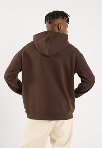 Bruine hoodie met een zachte textuur en een relaxte pasvorm, voorzien van een kangoeroezak en ribgebreide manchetten en zoom.