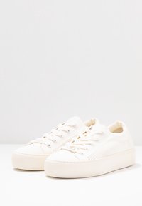 Białe płótno trampki z teksturowanym bokiem, okrągłym noskiem, płaskimi sznurówkami i platformą. Gładka powierzchnia z delikatnymi detalami przeszyć.