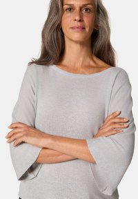 Lichtgrijze top met lange mouwen, voorzien van een wijd decolleté en uitlopende mouwen. De stof heeft een gladde, gebreide textuur.