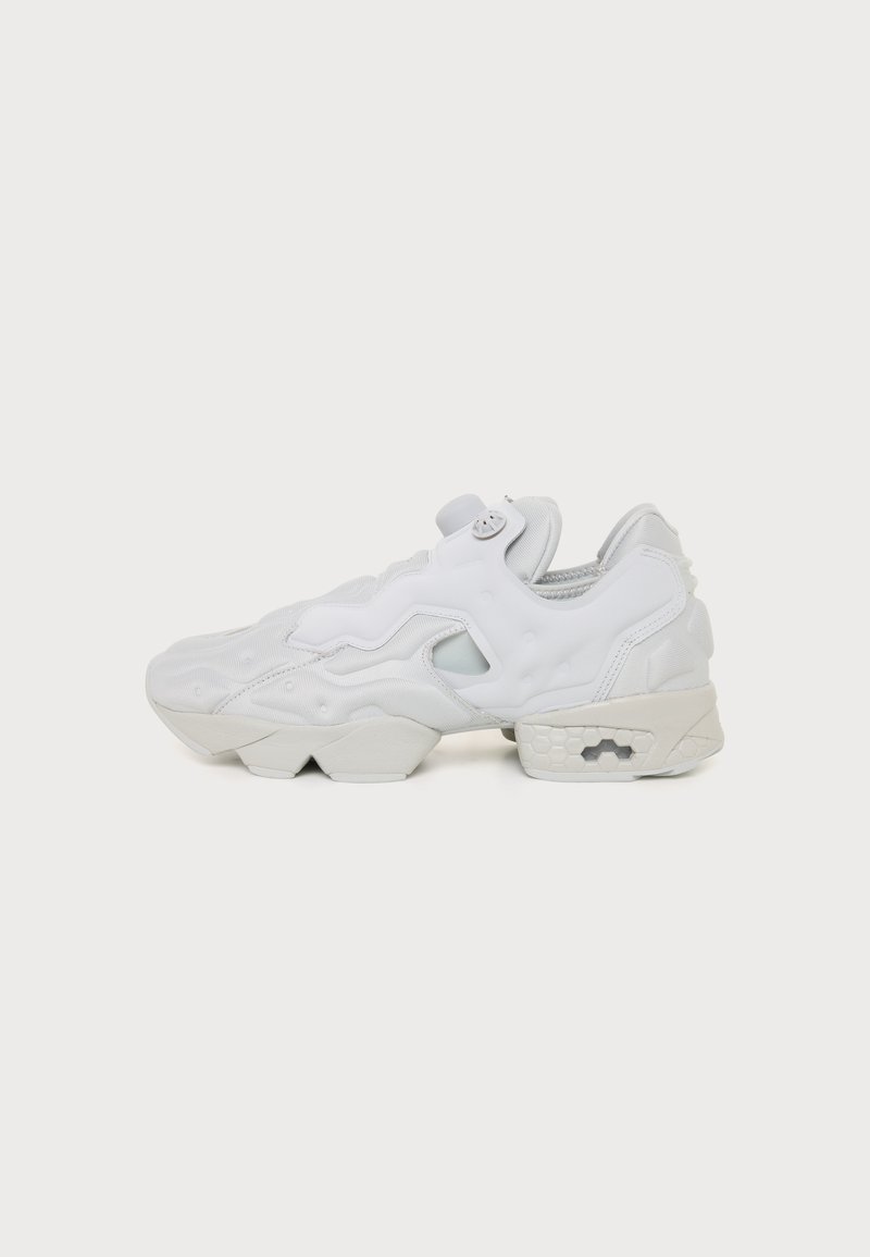 Baskets futuristes blanches avec semelle sculptée, détail découpé sur le côté et tige sans couture, vues de profil sur un fond uni.