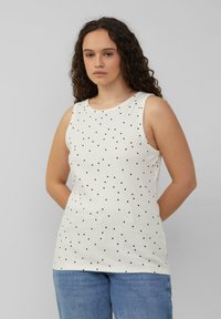 Witte mouwloze top met een ronde hals, voorzien van een patroon van kleine zwarte stippen, gemaakt van lichtgewicht stof, gecombineerd met lichtblauwe jeans.