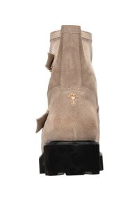 Stivale alla caviglia in suede beige con suola nera spessa, due fibbie laterali e un piccolo emblema dorato sul tallone.