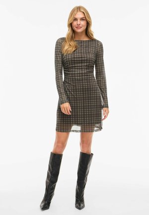Long-sleeve plaid dress in earthy tones, featuring a fitted silhouette with a side slit and smooth, slightly sheer fabric. Paired with black knee-high boots.
