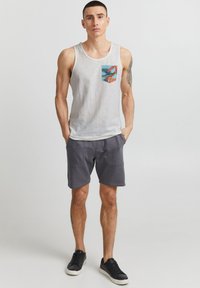 Top gri cu un design colorat al buzunarului, asociat cu pantaloni scurți gri închis și adidași negri. Stil sportiv simplu și lejer.