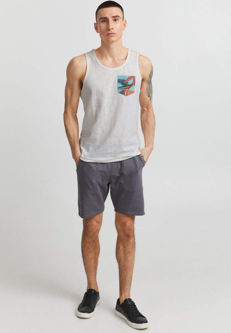 Top gri cu un design colorat al buzunarului, asociat cu pantaloni scurți gri închis și adidași negri. Stil sportiv simplu și lejer.
