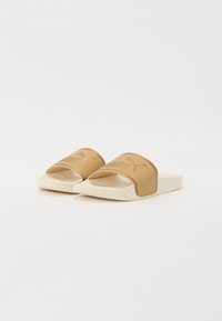 Sandaalit, joissa on beige synteettinen hihna, jossa on logo, kermaisen värinen kumipohja, lattiadesign ja sileä pinta.