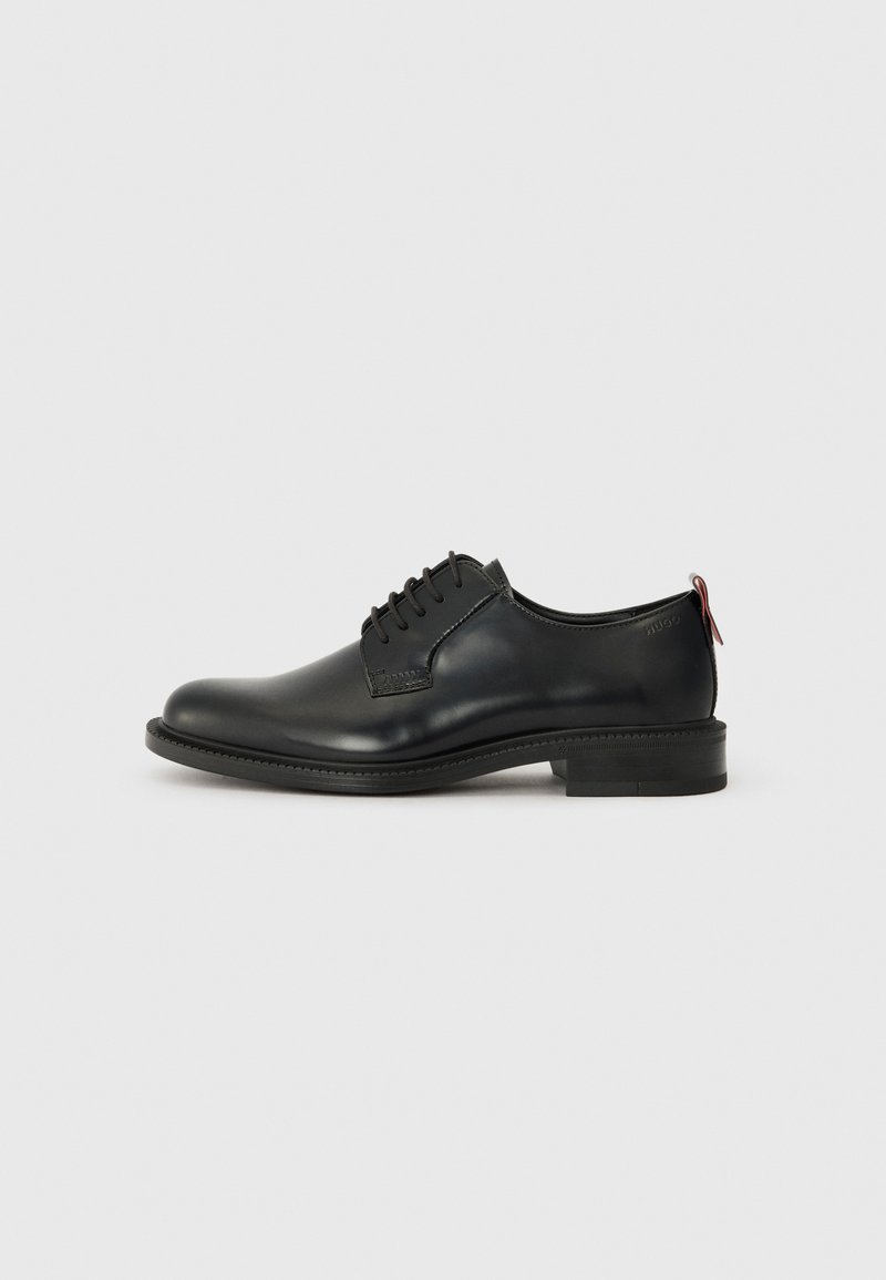 Black leather oxford shoe with a smooth finish, lace-up design, round toe, and a low stacked heel. Features a contrasting red pull tab.