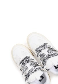 Baskets blanches avec un dessus en cuir texturé et en maille, comprenant des lacets à motif zigzag noir et blanc et une semelle en caoutchouc beige.