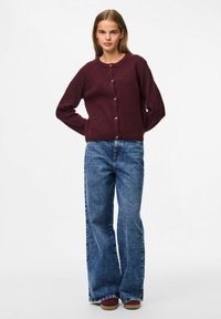 Burgundijas adīta džemperis ar apaļu kakla izgriezumu un piecu pogu aizdari, apvienots ar augsta vidukļa zilā platā kāju džinsiem.