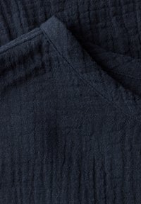 Tessuto di un blu scuro, texture lavorata con un motivo intrecciato, presenta una superficie morbida e stropicciata con cuciture visibili lungo i bordi.