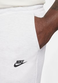 Baltas kokvilnas sporta bikses ar melnu Nike logo priekšā. Iekļauj sānu kabatu ar tīru, vieglu apdari.