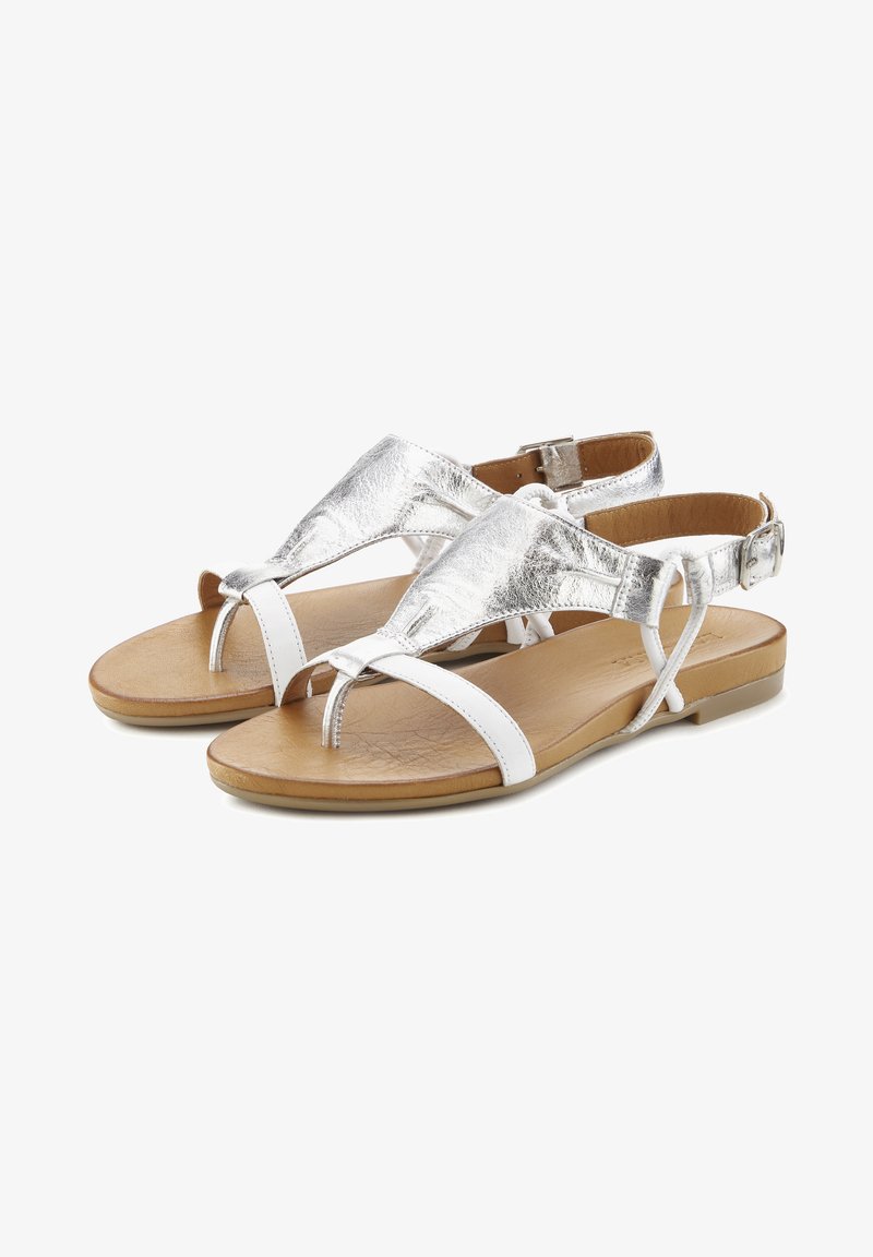 Metalne srebrne in bele ravne sandale z medsebojno prepletenimi trakovi, T-bar obliko in svetlo rjavo teksturirano podplato. Nastavljiv zaponko za gleženj.
