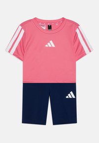 Ružová atletická košeľa s bielymi akcentmi a logom, spárovaná s námořníckymi šortkami s bielym logom. Vyrobená z ľahkého, priedušného materiálu.