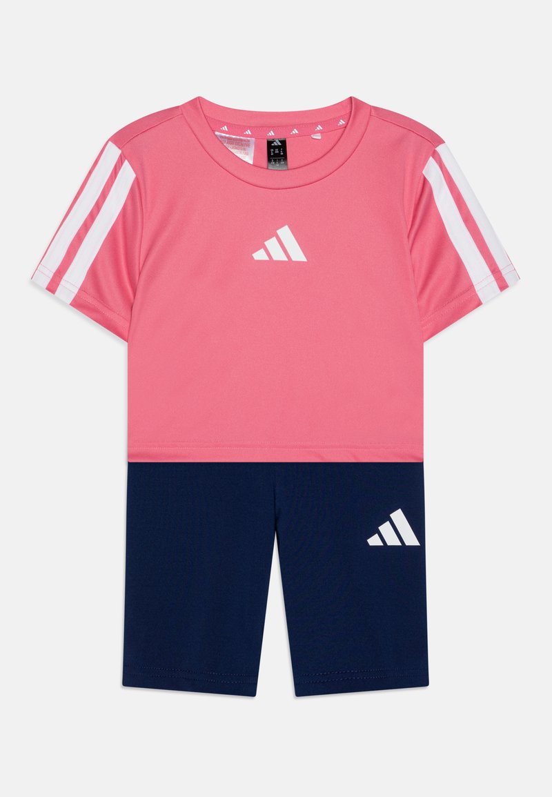 Camiseta deportiva rosa con acentos y logotipo blancos, combinada con pantalones cortos azul marino que presentan un logotipo blanco. Fabricada con material ligero y transpirable.