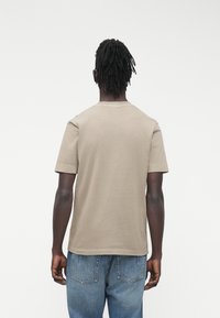 Khaki bavlněné tričko s klasickým střihem a krátkými rukávy. Jednoduchý kulatý výstřih a hladké, ploché švy. Nošeno s modrými džínami.