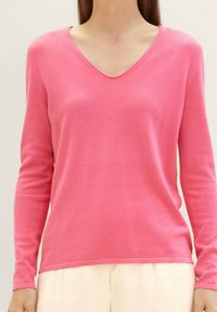 Rosa Pullover mit langen Ärmeln und V-Ausschnitt, mit glatter Textur und gerippten Details entlang des Halsausschnitts und Saums. Leichter Stoff.