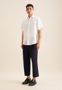 Witte kortemouw overhemd met knopen, relaxte pasvorm, gecombineerd met marineblauwe cropped broek en zwarte leren schoenen. Gladde textuur, minimalistisch ontwerp.