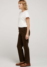 T-shirt blanc à manches courtes associé à un pantalon en velours côtelé marron. Des mocassins marron avec des accents tissés complètent la tenue. Design simple et ajusté.