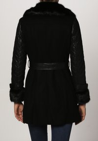 Zwarte jas met een faux fur kraag en manchetten, gevoerde zwart leren mouwen en een ceinture tailleontwerp. Glad textuur overal.