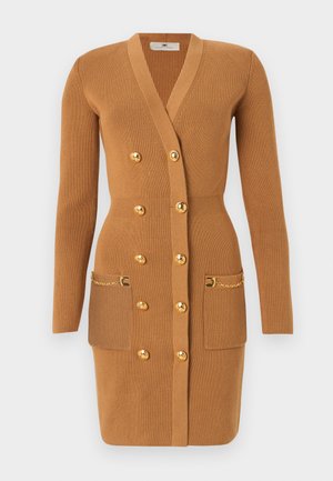 Kamelfarvet knælængde ribstrikket cardigan-kjole med lange ærmer, dobbeltradede guldbetjente knapper og forlommer med guldkædeudsmykning.