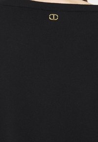 T-shirt noir avec un col rond et un petit logo doré à l'arrière, fabriqué dans un tissu lisse et léger.